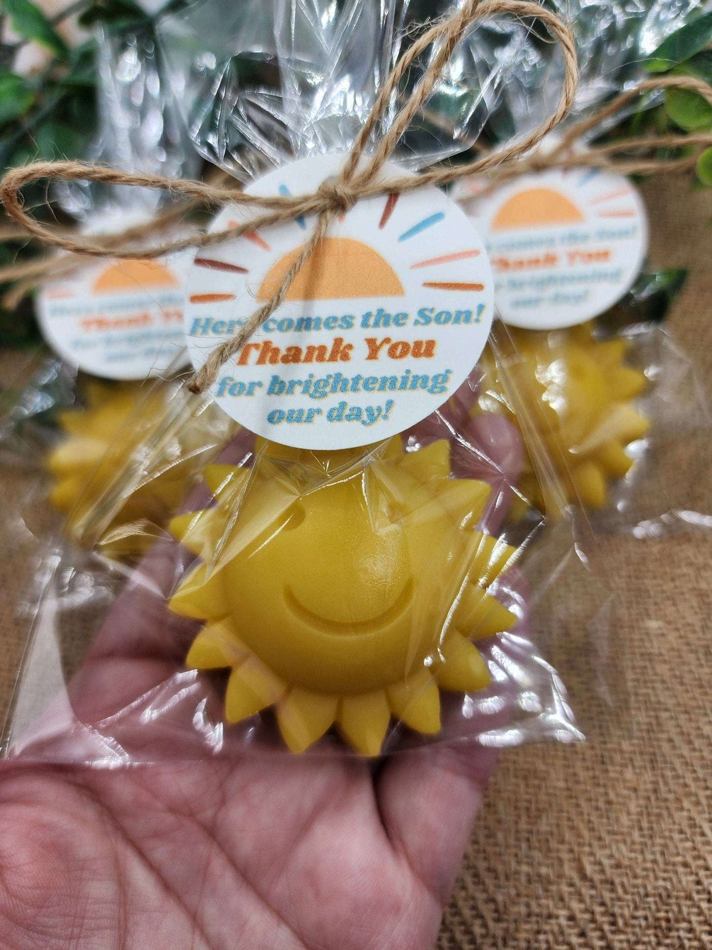 Yellow sun-shaped item with a 'Thank You' tag, held by a hand against a textured surface.