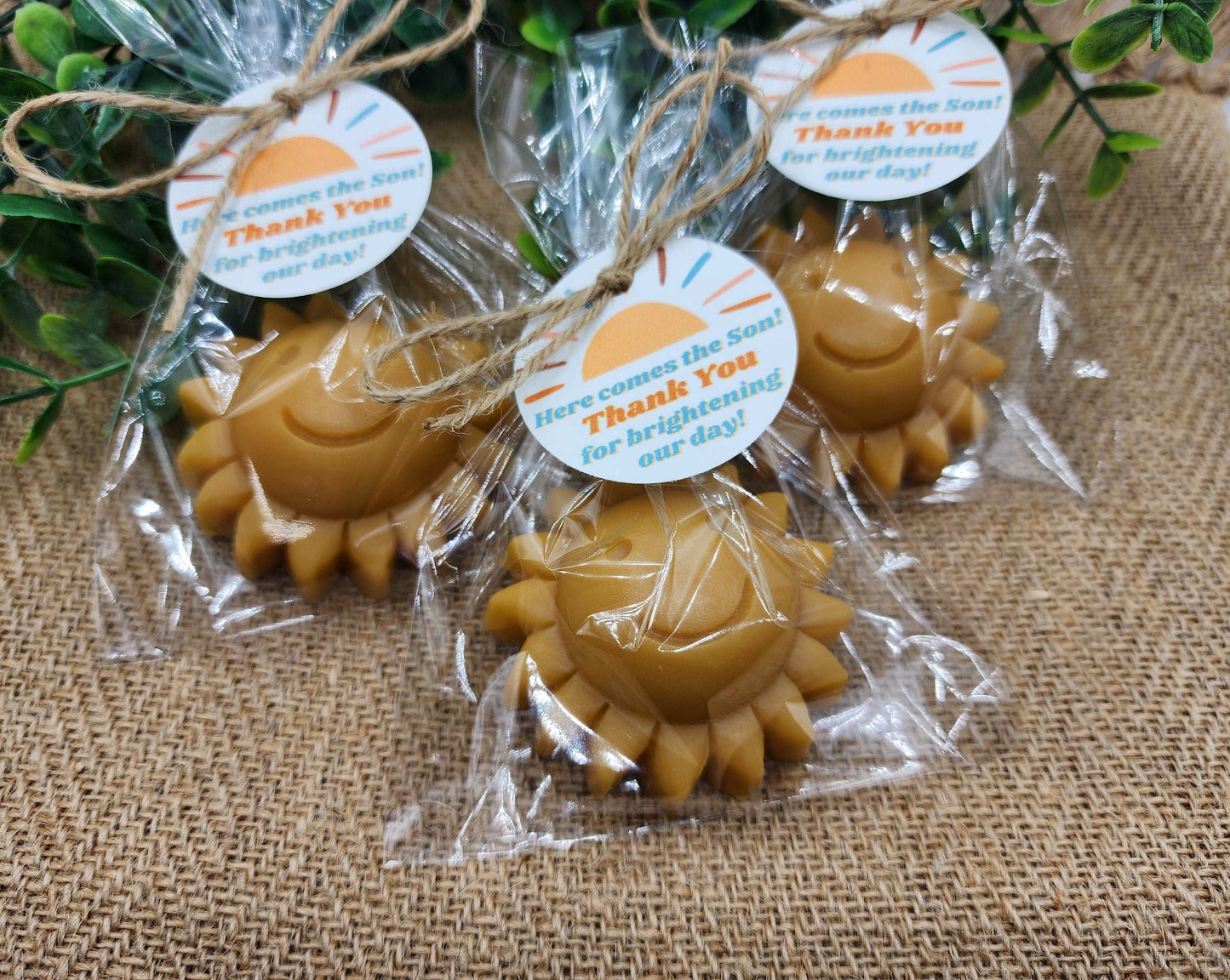 Sun-shaped candles in clear packaging with tags on a textured surface
