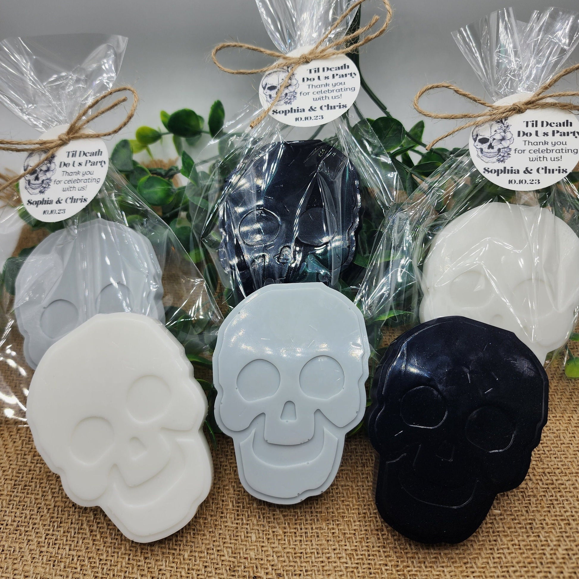 Skull-shaped soaps in clear packaging with decorative ribbons on a textured surface.