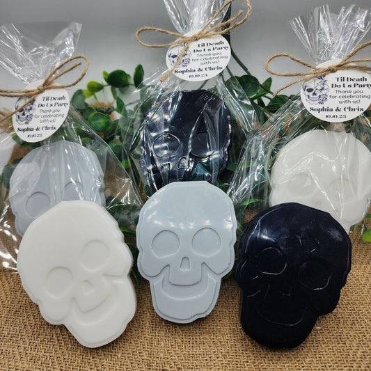 Skull-shaped soaps in clear packaging with decorative ribbons on a textured surface.