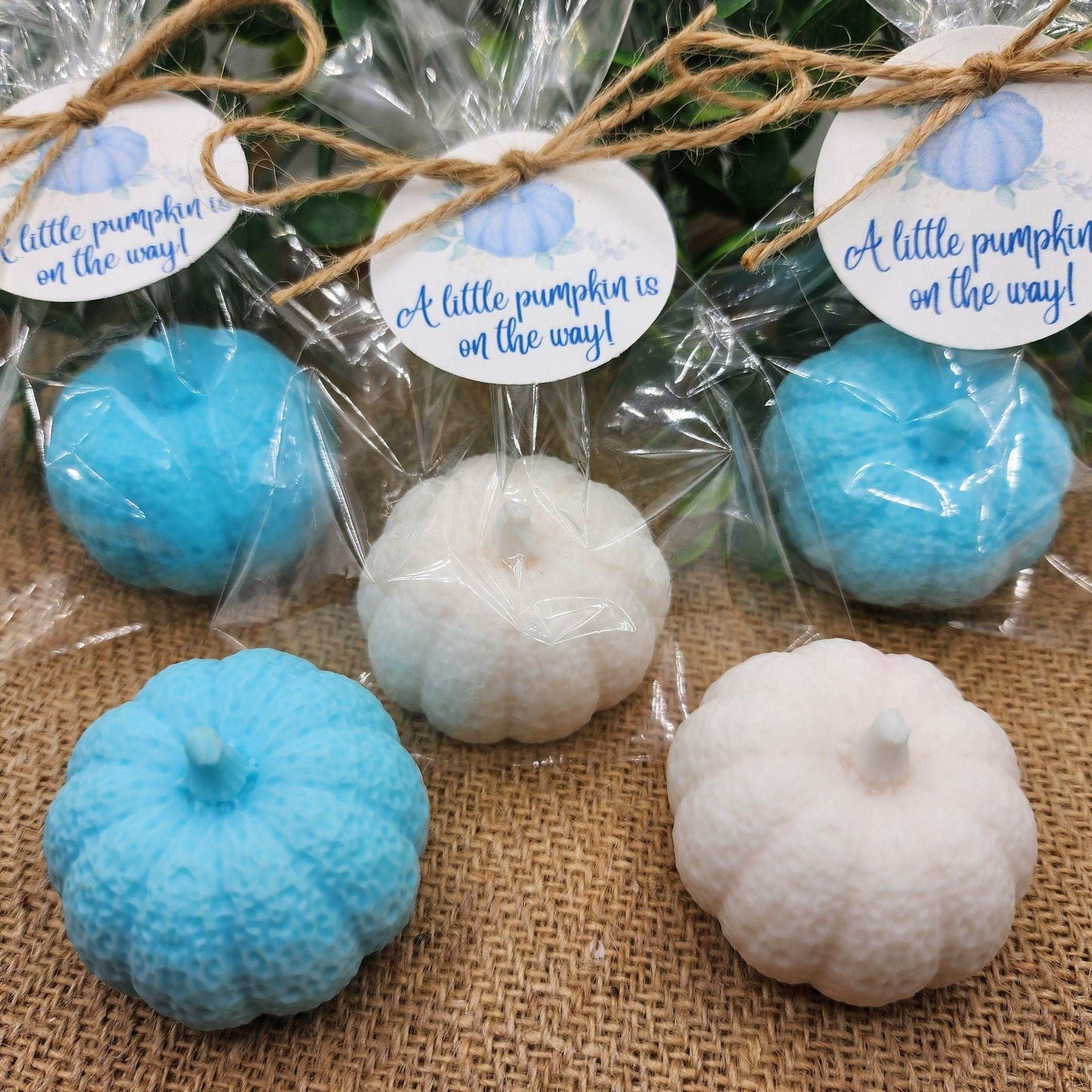 Decorative pumpkins in blue and white with 'A little pumpkin is on the way!' labels on a burlap surface.