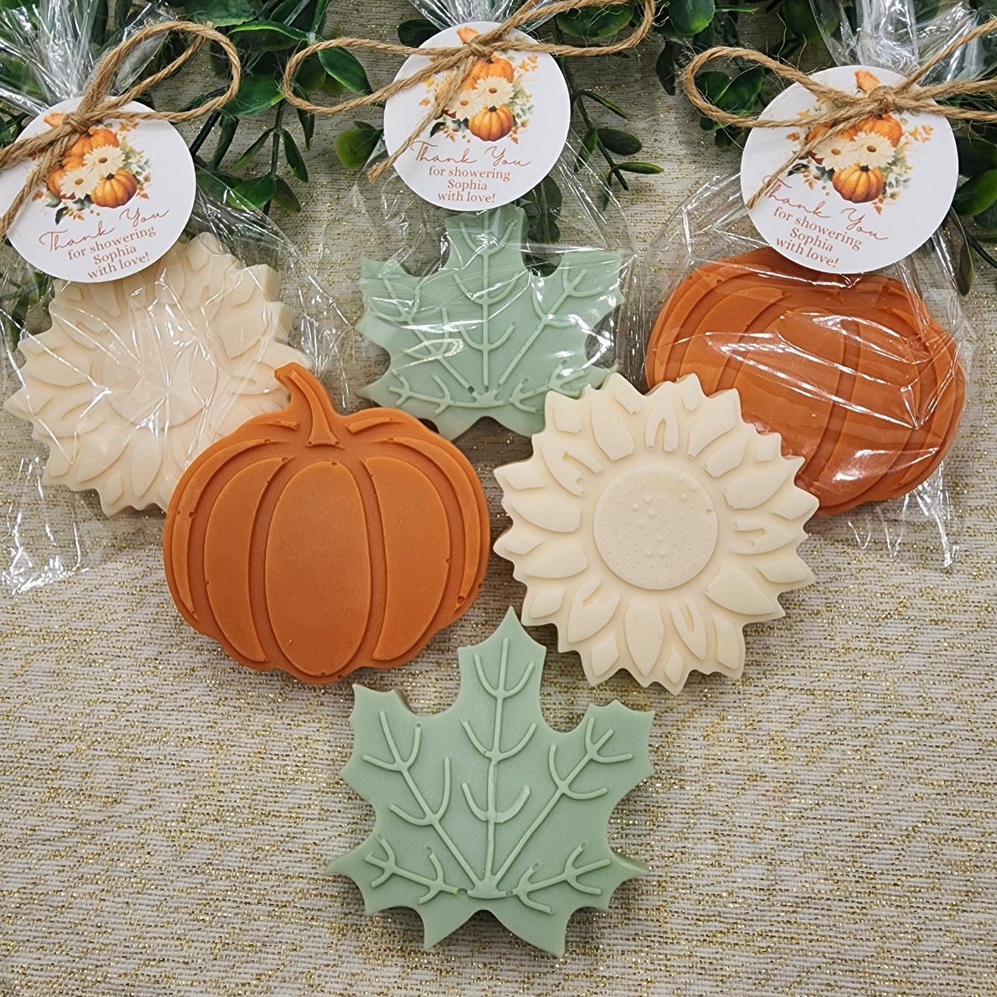 Decorative soap bars shaped like pumpkins, leaves, and sunflowers on a textured surface with decorative tags.