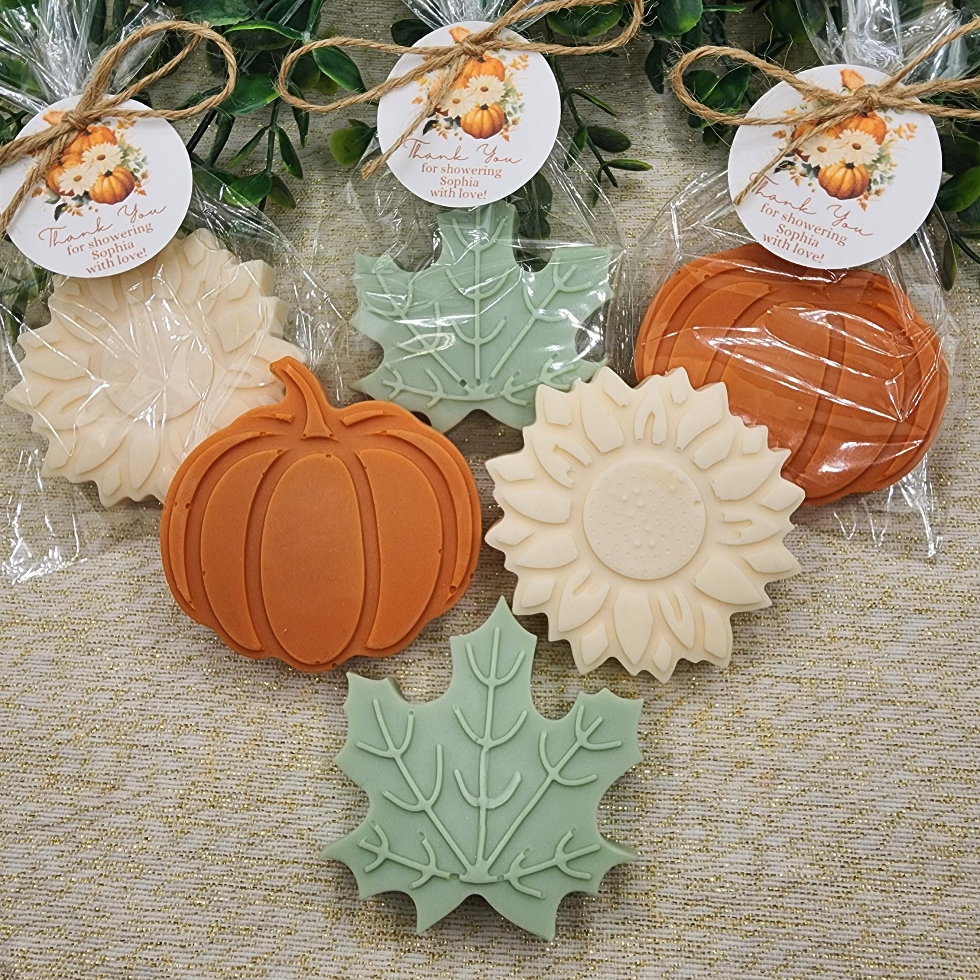 Decorative soap bars shaped like pumpkins, leaves, and sunflowers on a textured surface with decorative tags.