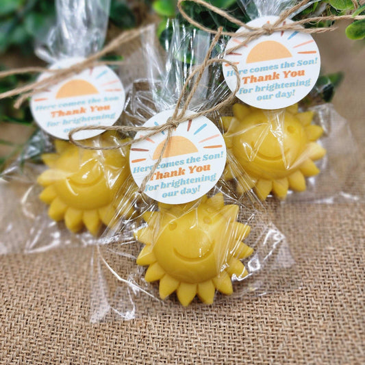Sun-shaped yellow favors in clear packaging with 'Here Comes the Sun' tags on a textured surface.