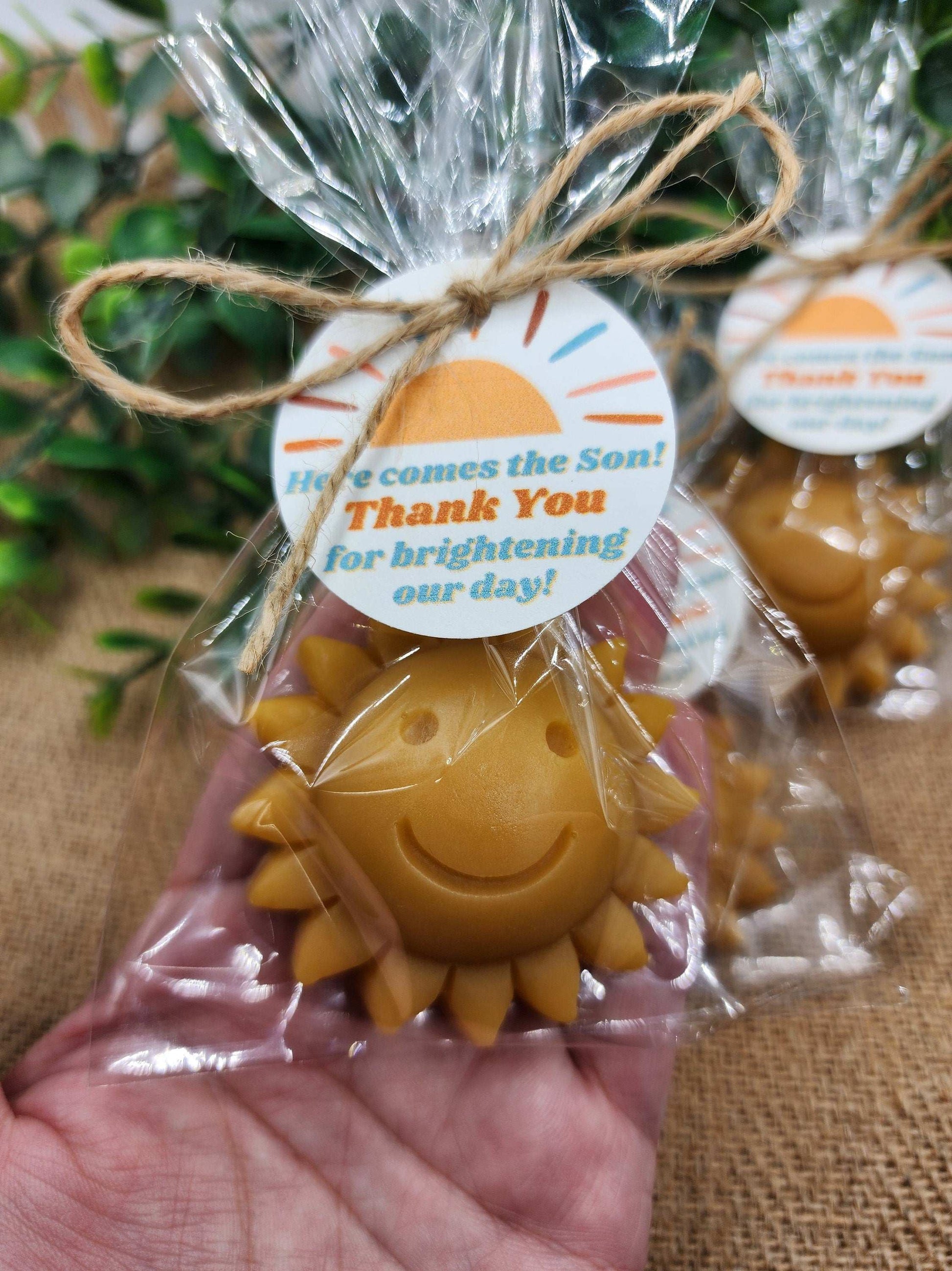Sun-shaped favor in clear packaging with a decorative tag, held by a hand.