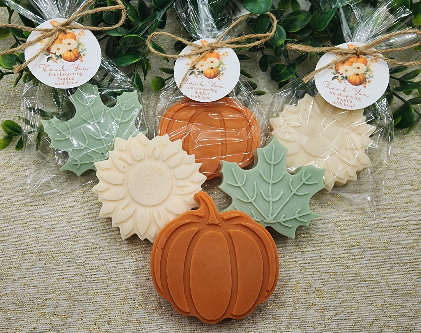 Decorative soap bars shaped like pumpkins, leaves, and sunflowers with clear packaging on a textured surface.
