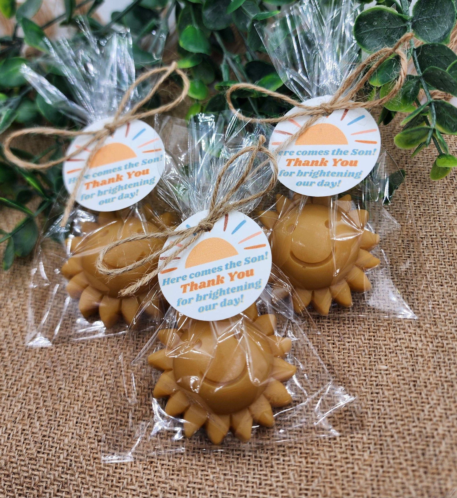 Sun-shaped candles in clear packaging with decorative tags on a textured surface.
