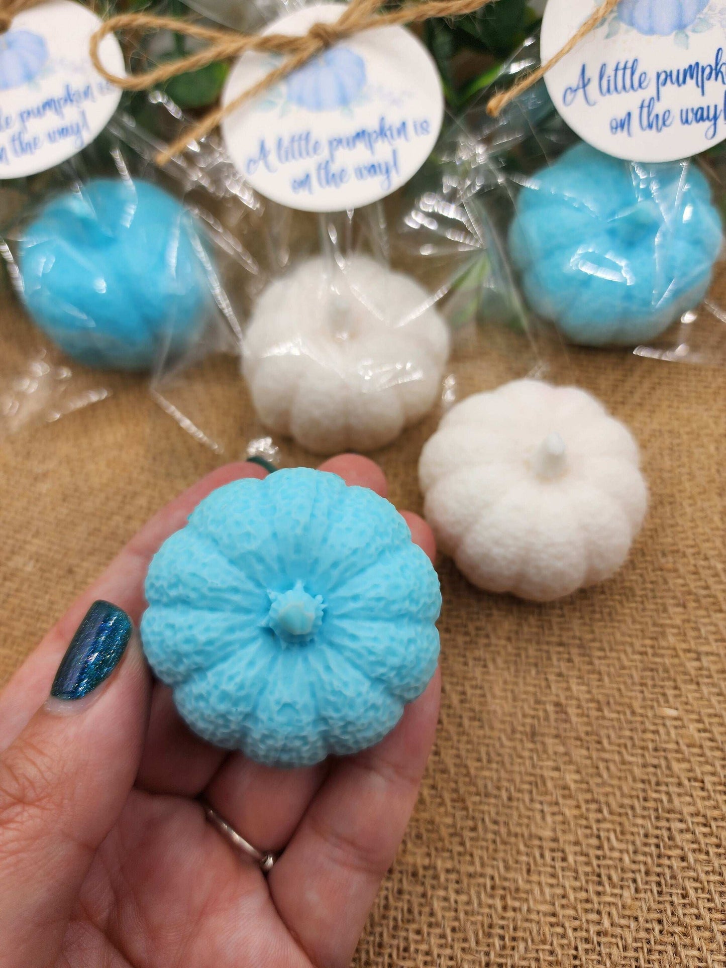 Blue and white decorative pumpkins with 'a little pumpkin is on the way' labels on a textured surface.